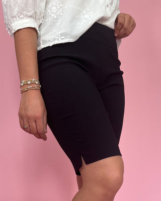 Person wearing a white top with lace details and black shorts on a pink background