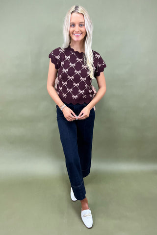 Burgundy knit top with scalloped edges and pink bow pattern styled with dark wide leg cropped jeans and white loafers