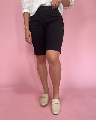 Person wearing black shorts and white shoes on a pink background