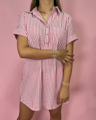 Person wearing a red and white striped dress against a pink background