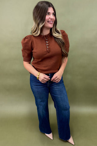 Woman wearing a brown top and blue jeans against an olive green background