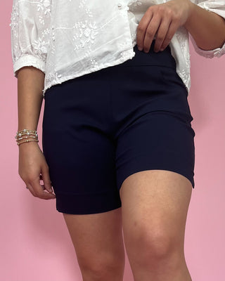 Person wearing navy shorts and a white lace top on a pink background