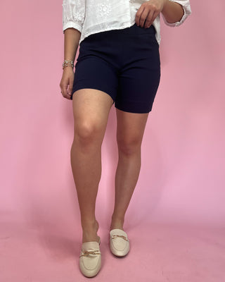 Person wearing navy shorts and a white top on a pink background