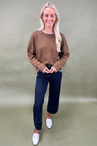 Woman wearing a brown sweater, dark jeans, and white loafers on a green background
