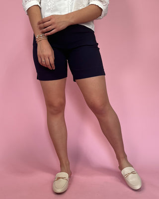Person wearing navy shorts and white loafers on a pink background
