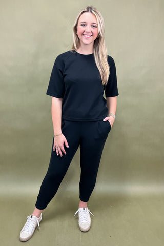 Woman wearing a black outfit with white sneakers against a green background