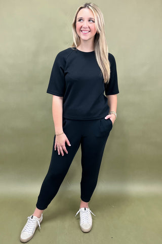 Woman wearing a black outfit with white sneakers against a green background