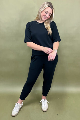 Woman wearing a black outfit with white sneakers on a green background