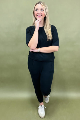 Woman wearing a black outfit with white sneakers against a green background