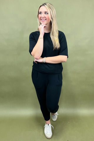 Woman wearing a black outfit with white sneakers against a green background