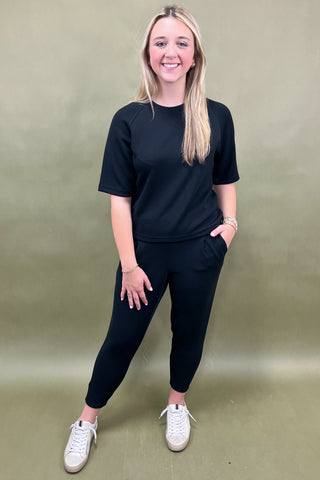 Woman wearing a black outfit with white sneakers against a plain background