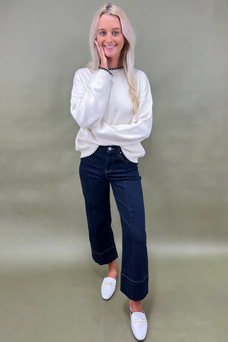 Woman wearing a white sweater and dark jeans against a green background