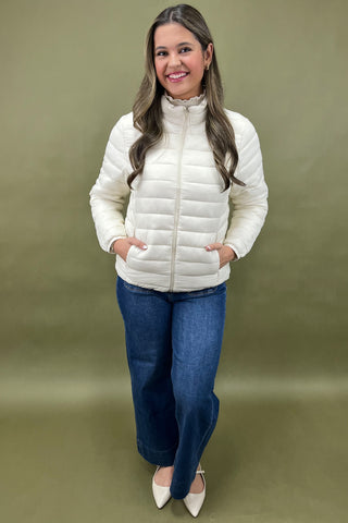 Woman wearing a white puffer jacket and blue jeans against a green background