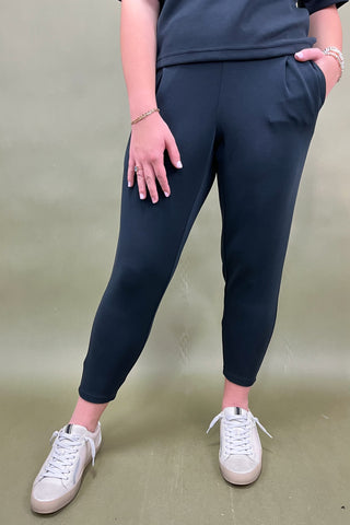 Person wearing navy jogger pants and white sneakers on a plain background