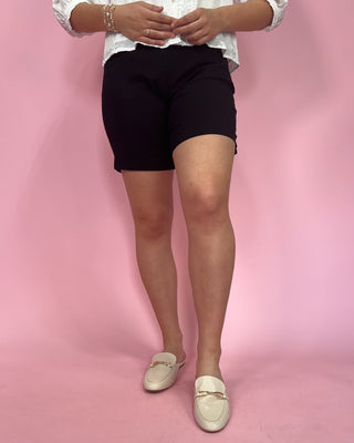Person wearing black shorts and white shoes on a pink background