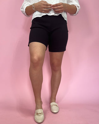 Person wearing black shorts and a white top on a pink background