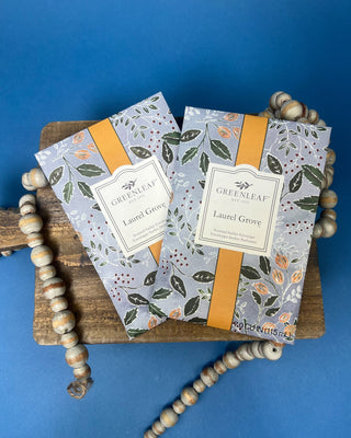 Greenleaf Laurel Grove scented sachet displayed on a rustic wooden board with decorative wooden beads.