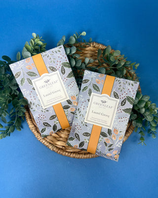 Greenleaf Laurel Grove scented sachet displayed on a rustic wooden board with decorative wooden beads.
