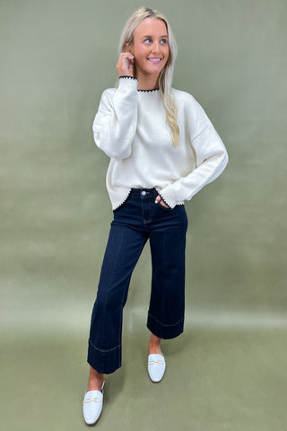 Woman wearing a white sweater and dark jeans against a green background