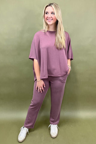 Woman wearing a mauve outfit with white sneakers against an olive green background