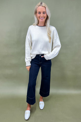 Woman wearing a white sweater and dark jeans against a green background