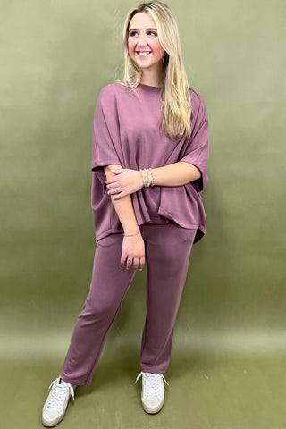 Woman wearing a mauve outfit with white sneakers against a green background