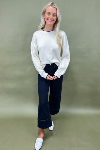 Woman wearing a white sweater and dark jeans against a green background