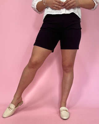 Person wearing black shorts and white shoes on a pink background