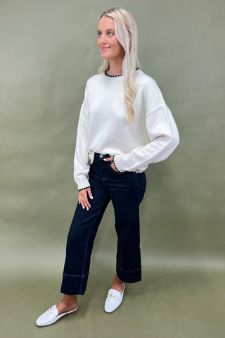 Woman wearing a white sweater and dark jeans against a green background