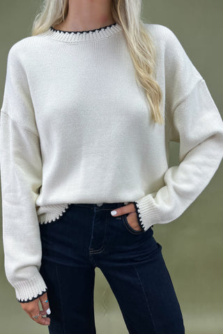 Woman wearing a white sweater and dark jeans against a green background