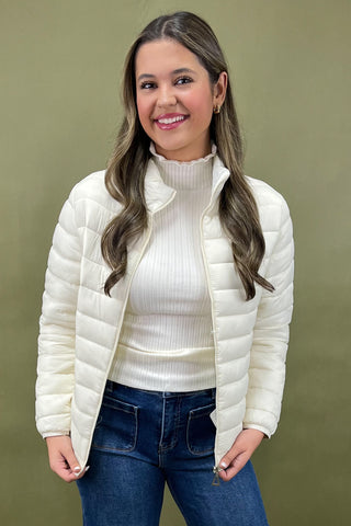 Woman wearing a white puffer jacket over a white sweater with blue jeans on a green background
