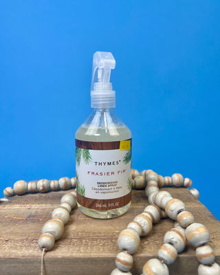 Thymes Frasier Fir 9 oz. Deodorizing Linen Spray displayed against a solid blue background.