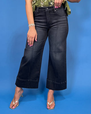 A person wearing dark charcoal cropped wide-leg denim jeans with a green