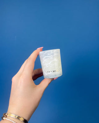 Frasier Fir Tidings Votive Candle in frosted marbled glass against a solid blue background. 