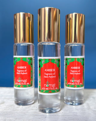 Nemat Amber fragrance oil roll-on in a clear glass bottle with a decorative red and green label and gold cap.