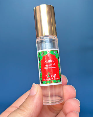 Nemat Amber fragrance oil roll-on in a clear glass bottle with a decorative red and green label and gold cap.