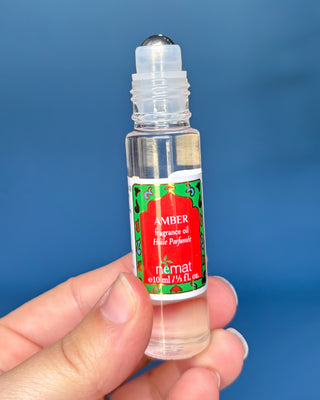 Nemat Amber fragrance oil roll-on in a clear glass bottle with a decorative red and green label and gold cap.