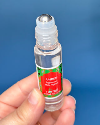 Nemat Amber fragrance oil roll-on in a clear glass bottle with a decorative red and green label and gold cap.