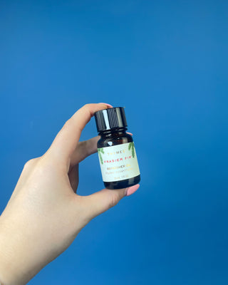 Thymes Frasier Fir Refresher Oil in amber glass bottle with signature evergreen label displayed on a solid blue background.