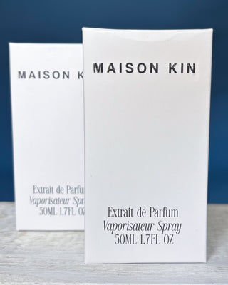 Two Maison Kin perfume bottles on a wooden surface with a blue background