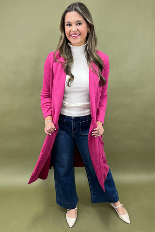 Woman wearing a pink coat, white shirt, blue jeans, and white shoes on a green background