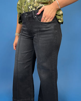 A person wearing dark charcoal gray wide-leg jeans, paired with an olive green floral top