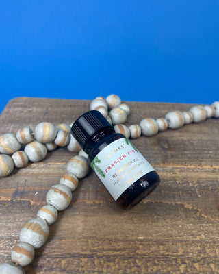 Thymes Frasier Fir Refresher Oil in amber glass bottle with signature evergreen label displayed on a solid blue background.