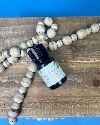 Thymes Frasier Fir Refresher Oil in amber glass bottle with signature evergreen label displayed on a solid blue background.