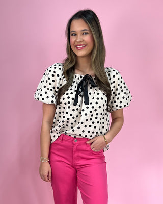 Woman wearing a polka dot blouse and pink pants against a pink background