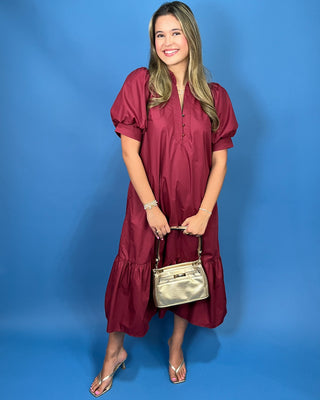A woman modeling a short-sleeve midi dress in deep burgundy with puff sleeves, a buttoned neckline, and a ruffled hem