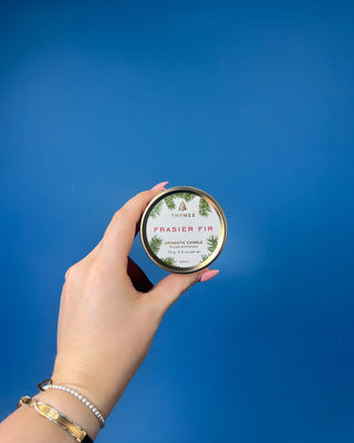 Thymes Frasier Fir Travel Tin Candle displayed on a solid blue background. 