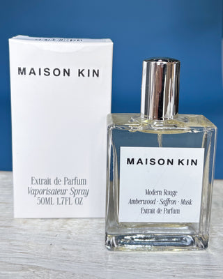 Maison Kin perfume bottle and packaging on a wooden surface with a blue background