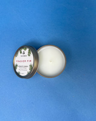 Thymes Frasier Fir Travel Tin Candle displayed on a solid blue background. 