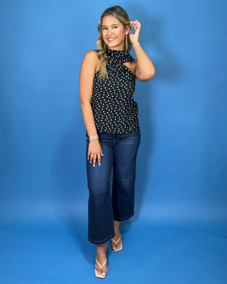 Black and white polka dot sleeveless top with a draped high neckline, gathered detail, and relaxed fit.